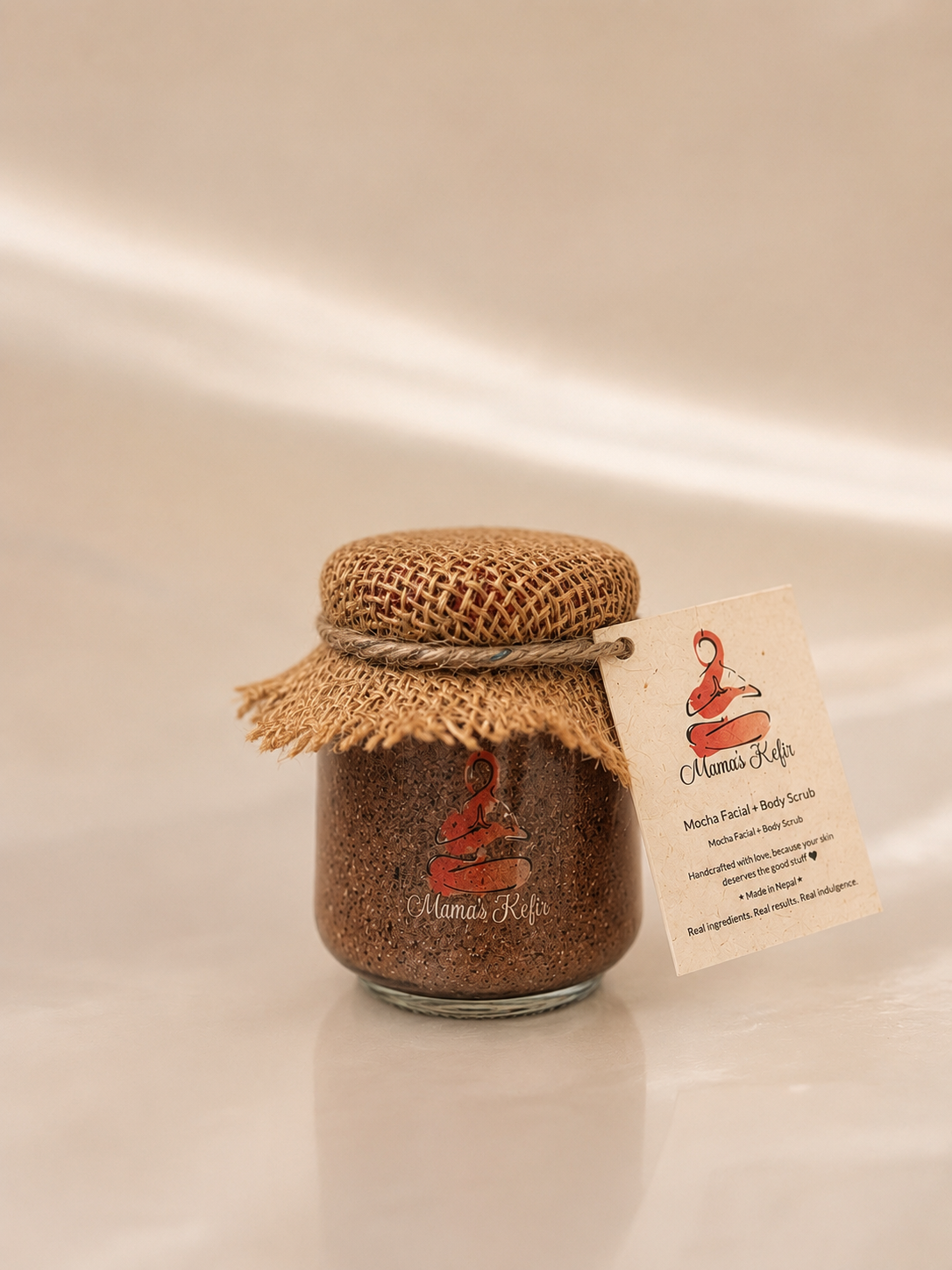 Mama's Kefir mocha coffee scrub jar with hessian lid resting on folded cream linen