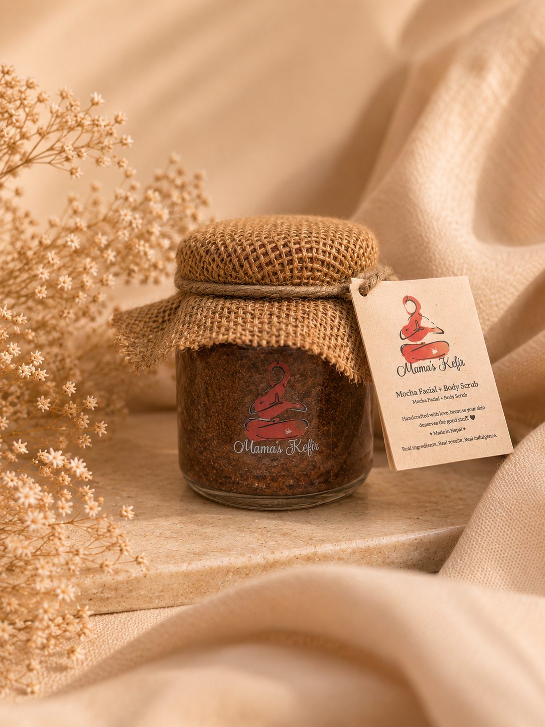 Mama's Kefir mocha coffee scrub jar with hessian lid resting on folded cream linen